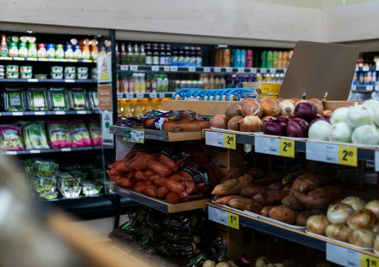 Rayon de fruits et légumes exotiques dans une épicerie, présentant des produits frais comme des patates douces, des bananes plantains et d'autres spécialités tropicales. L'image met en avant la diversité et la fraîcheur des produits. Sougou Express